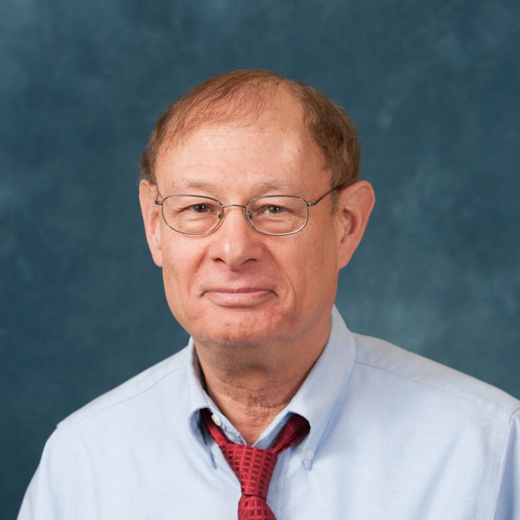 Photo of Mark Tessler wearing a blue shirt and red tie in front of a blue background. He is wearing glasses.
